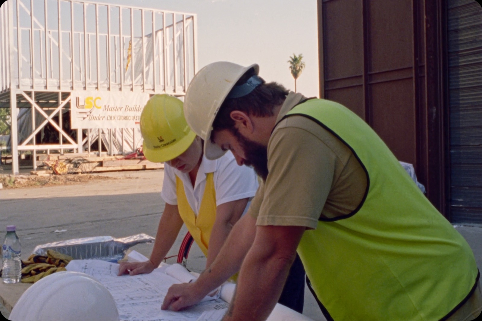 Two construction professionals reviewing blueprints at a job site table