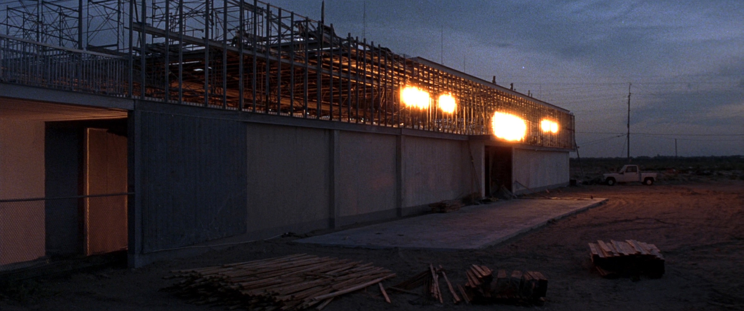 Steel-framed commercial building under construction at dusk with work lights glowing, Central Florida